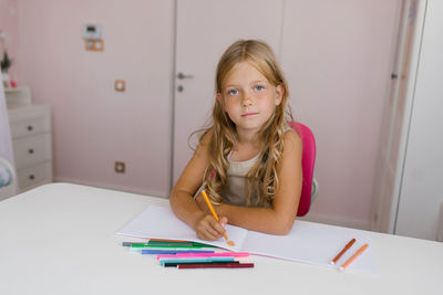 Schoolgirl with a pensively draws in a notebook with her right hand or does homework