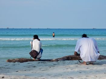 Rear view of couple standing at beach against clear sky