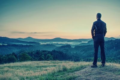 Man tourist traveler standing on hill side and looking to sunset, against backdrop of hills. 