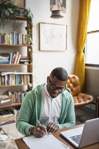 High angle view of man writing on paper while working at home