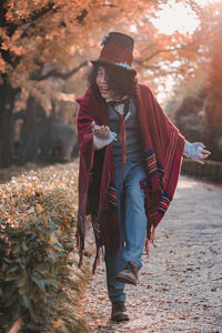 Man cosplaying mad hatter bowing on path next to hedges in autumn