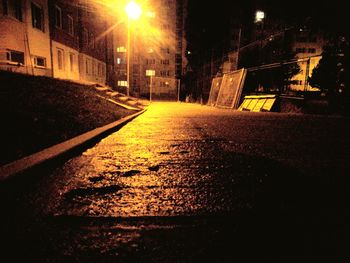 Wet street amidst illuminated buildings in city at night