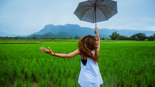 Woman with umbrella standing on field against sky