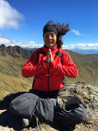 Young latin woman sitting doing yoga on a mountain top with blue sky on background