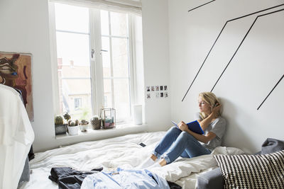 Full length of teenage girl reading book while resting on bed at home