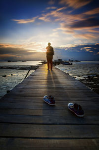Man standing on pier at sea against sky during sunset