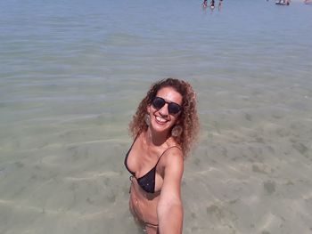 High angle view portrait of smiling woman taking selfie while standing at beach