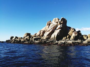 Rock formation in sea against clear blue sky