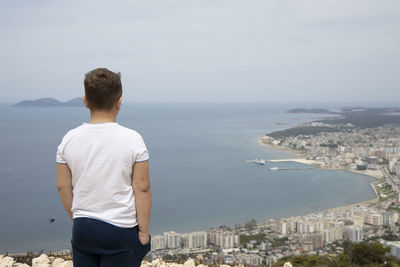 Rear view of man looking at cityscape against sky