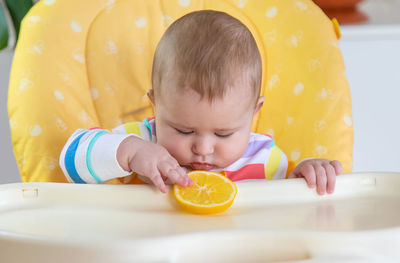Cute baby girl playing with orange fruit at home