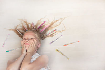 High angle view of girl lying on floor with pens
