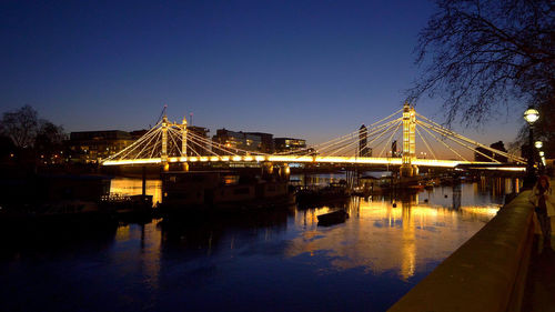 Illuminated pier over river against clear sky at dusk