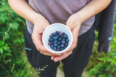 Midsection of person holding blueberries outdoors