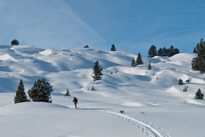 Man walking on snow covered land against sky