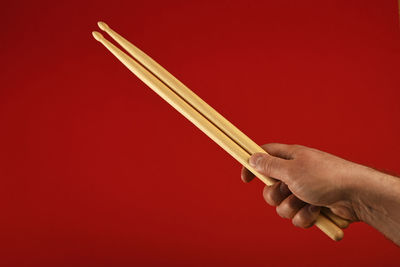 Cropped hand holding drumsticks against red background