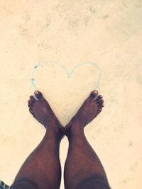 Low section of woman standing on heart shape on sand