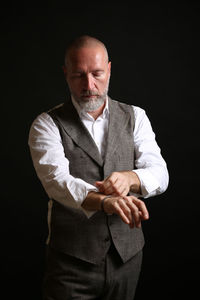 Mature businessman folding sleeve while standing against black background