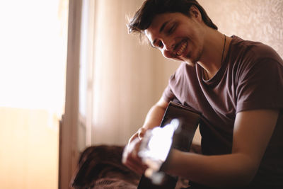 Happy young man playing guitar at home