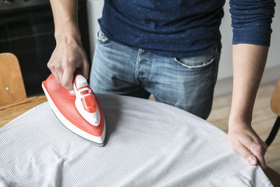 Midsection of man ironing shirt on table at kitchen