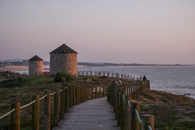 Wooden posts amidst sea and buildings against clear sky