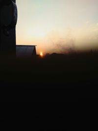 Silhouette buildings on field against sky during sunset