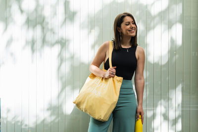 Satisfied female standing with eco friendly shopping bag in street in summer and looking away