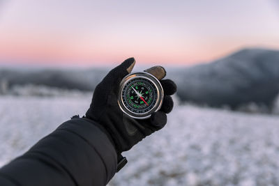 Close-up of explorer survival man holding a magnetic compass against sky during sunset.winter season
