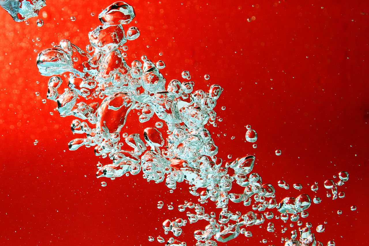 CLOSE-UP OF WATER SPLASHING ON RED BACKGROUND