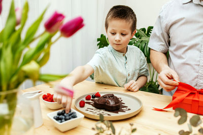 Dad and son decorate a heart-shaped cake with fresh berries and prepare a gift. mother's day