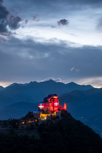Illuminated built structure on mountain against sky at dusk