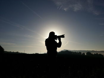 Silhouette man photographing against sky