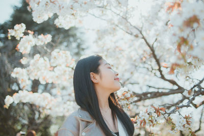 Young woman looking away while sitting on cherry tree