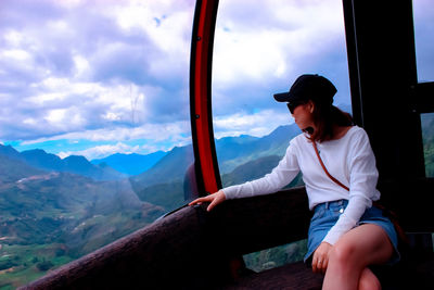 Woman sitting in overhead cable car against sky