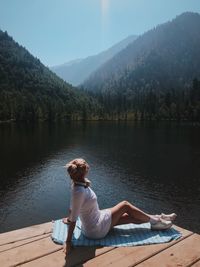 Woman sitting by lake against mountains