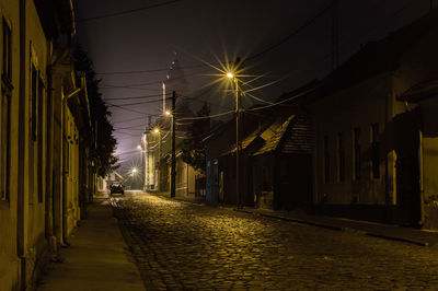 Empty footpath amidst illuminated street against sky at night