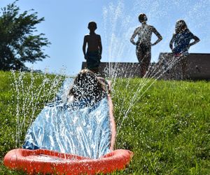 Girl enjoying in sprinkler with friends standing in background