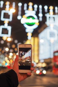 Man photographing illuminated mobile phone at night