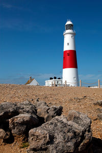 Lighthouse on rock by building against sky in red and white