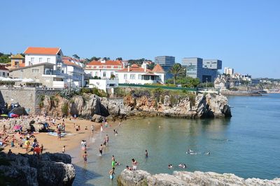 People on beach by city buildings against clear sky