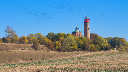 Lighthouse on field by building against clear sky