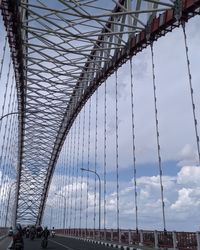 Low angle view of suspension bridge against cloudy sky