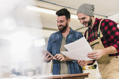 Two happy men with tablet looking at draft in workshop