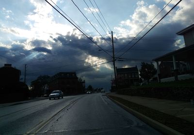 Road passing through city against cloudy sky