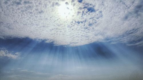 Low angle view of sunlight streaming through clouds