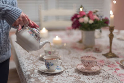 Midsection of woman pouring tea on table at home