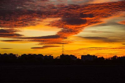 Silhouette of city against cloudy sky during sunset