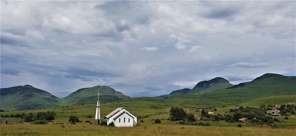 House on field by mountain against sky