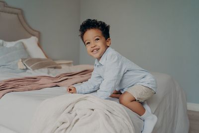 Portrait of smiling boy sitting on bed at home