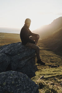 Man sitting on rock against sky