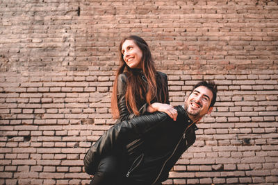 Portrait of young couple standing against brick wall